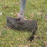 Spade pushed into the ground to make a slit perpendicular to another slit, forming a T shape